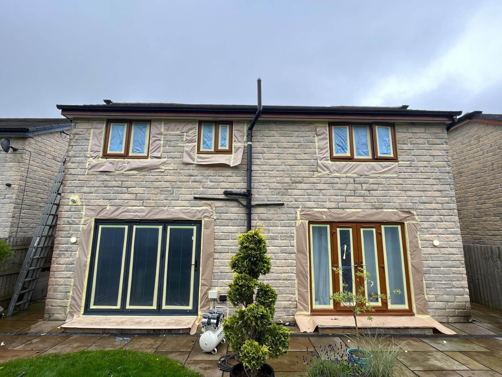 Stone house with bifold doors sprayed anthracite while other windows are masked up for spraying